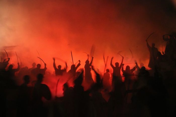 Die Silhouetten dutzender kriegerisch wirkender Menschen mit Beilen und Schwerten inmitten rot leuchtenden Rauchs zur Verbildlichung des Gedichts "Der Krieg" von Georg Heym